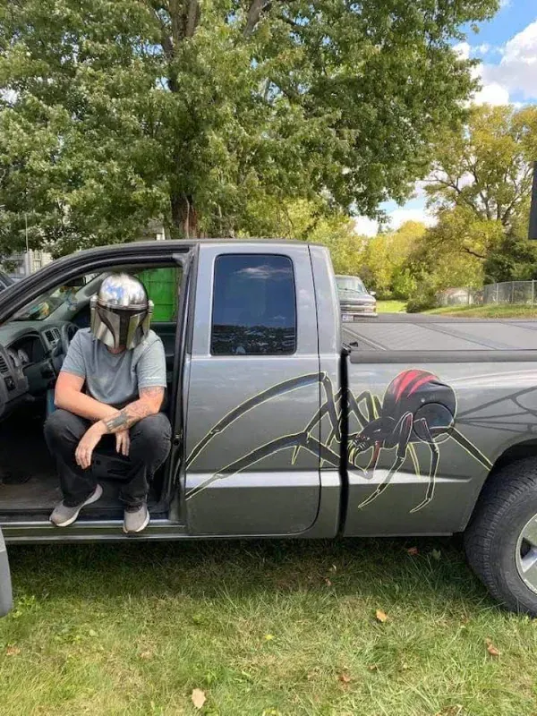 Person sitting on the open door of a gray pickup truck with a large spider decal on the side.