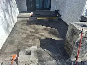 A stone patio under construction, with stacked bricks, tools, and a level resting on the blocks.