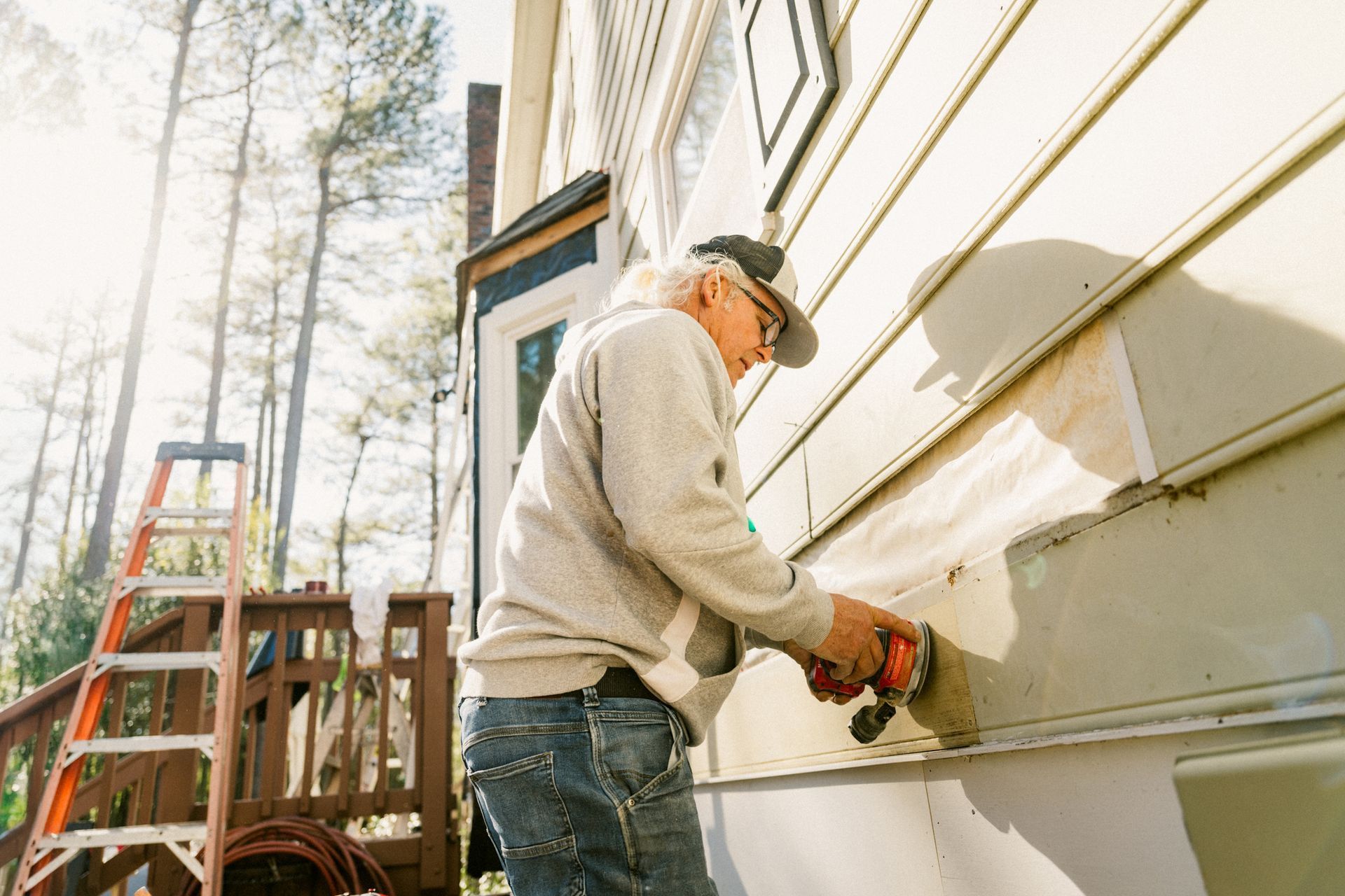 Person using a power tool on the side of a house, orange ladder nearby.