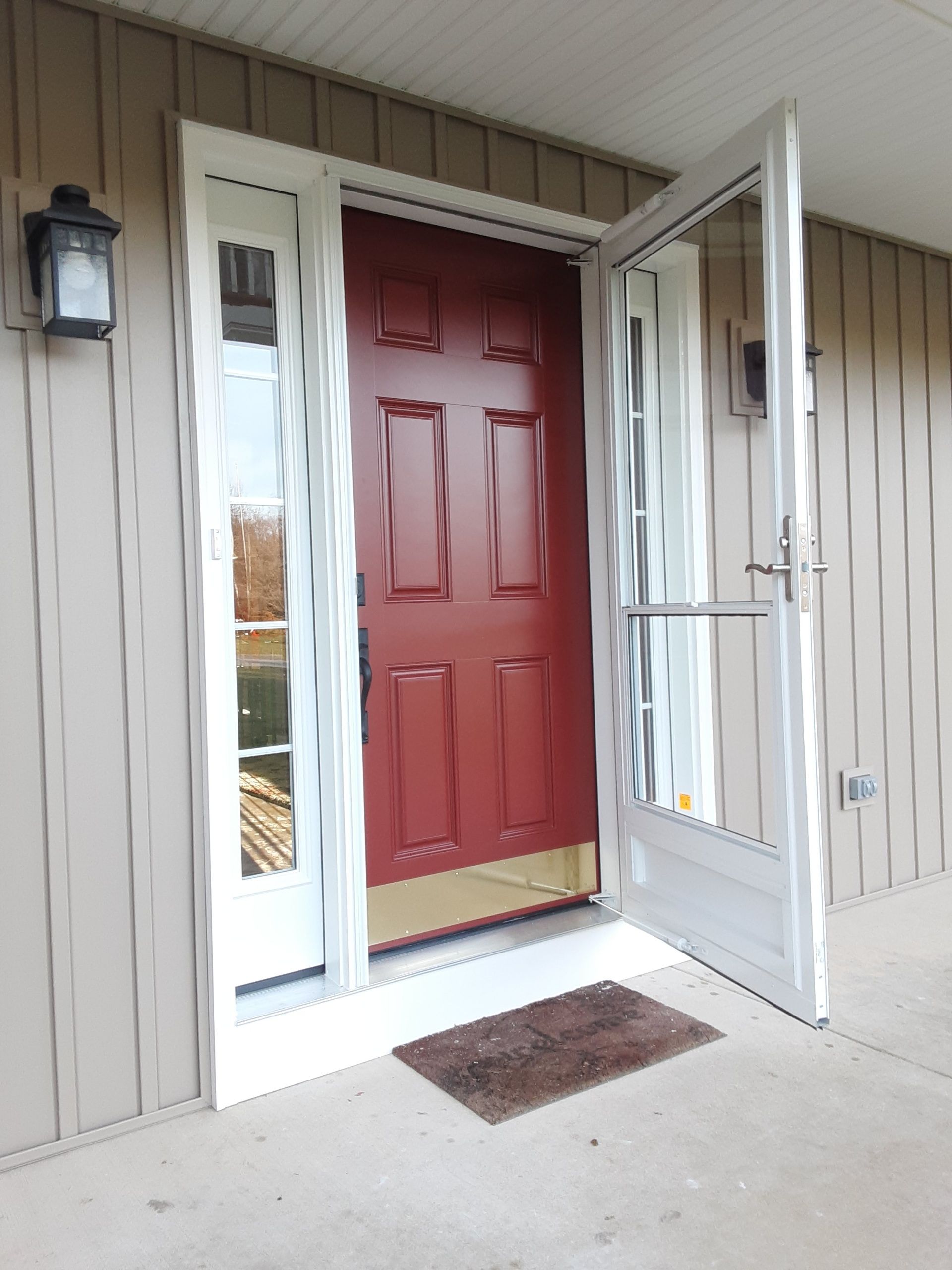 Open front door with red door, white trim, and sidelights
