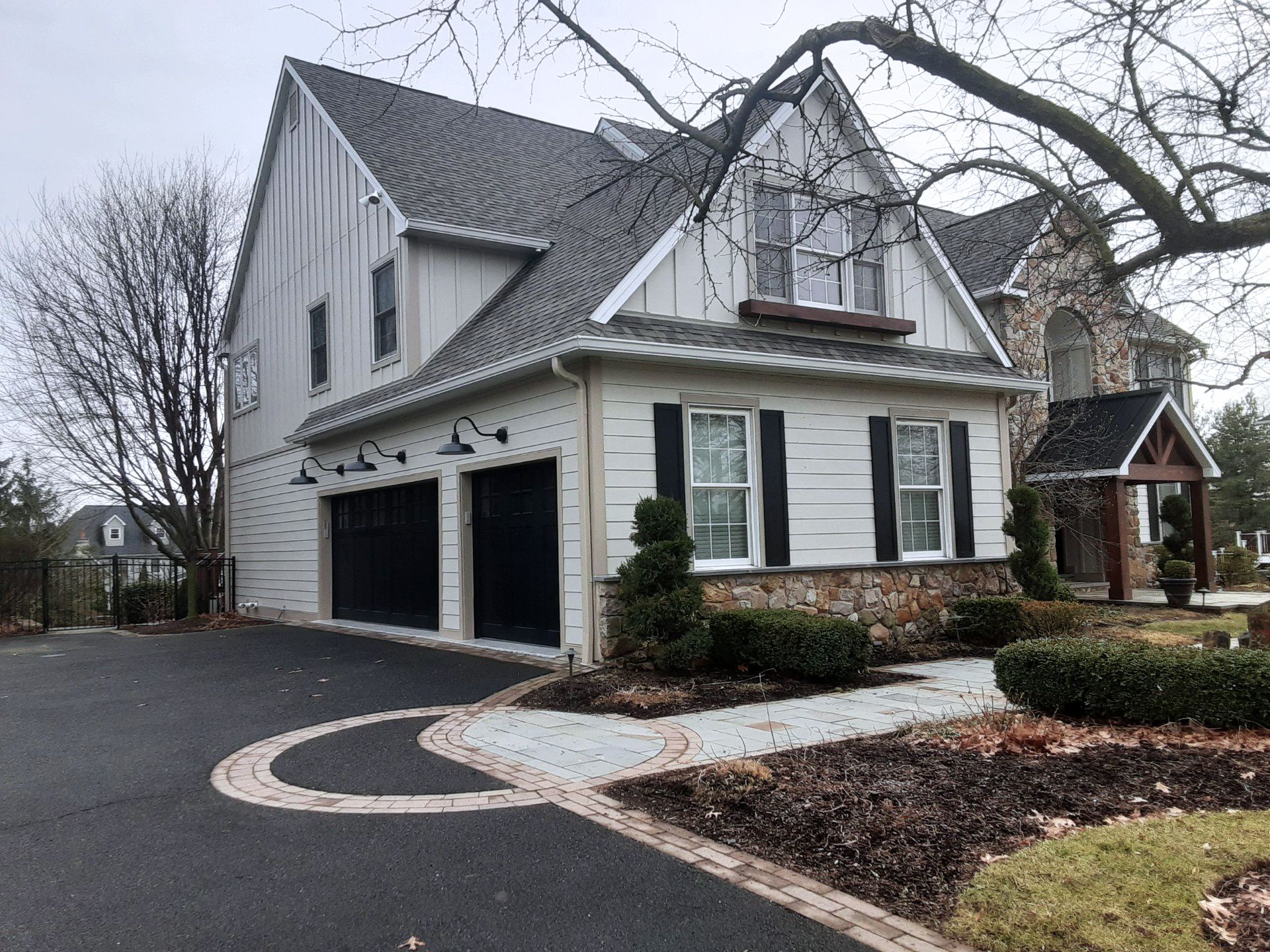 Two-story house with black shutters, garage, and curved driveway in a landscaped yard