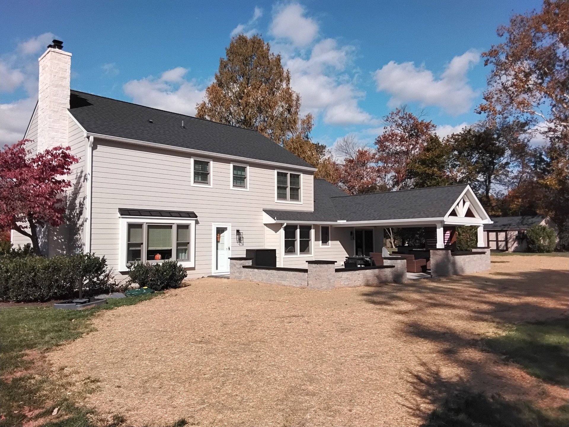 Two-story house with gray siding, black roof, and a gravel driveway under a partly cloudy sky.