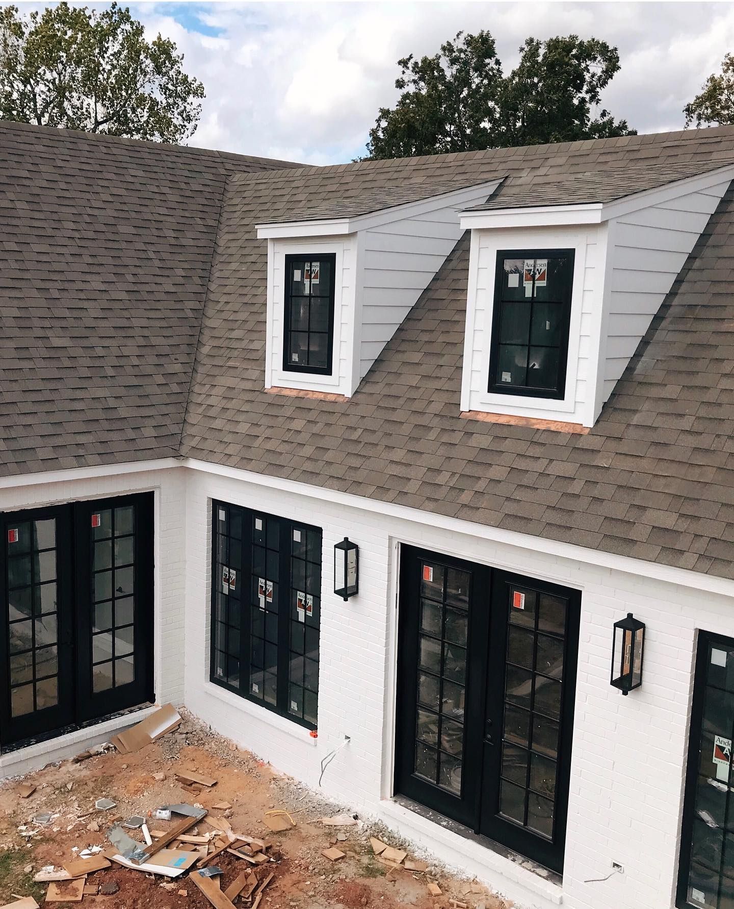 A white house exterior featuring a gray shingled roof, black-framed windows and doors, and two small roof dormers.