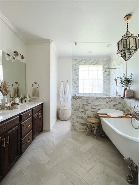 A modern bathroom with dark wood cabinets, a white claw-foot tub, a marble-tiled wall, and a geometric pendant light.