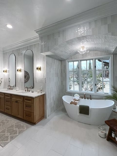 A luxurious bathroom with a white freestanding tub under a tiled arched window, alongside a wooden double vanity.
