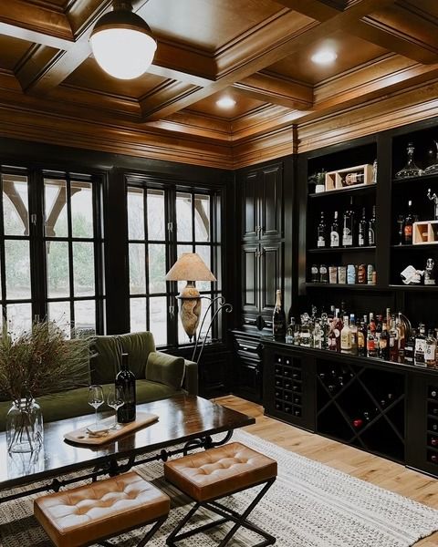 A luxurious home bar with dark cabinets, a green velvet sofa, a wooden coffee table, and an ornate coffered ceiling.