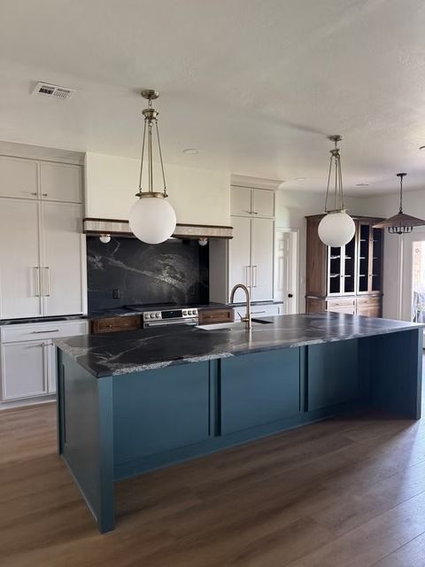 Modern kitchen with a blue island, dark marble countertops, off-white cabinetry, and globe pendant lights.