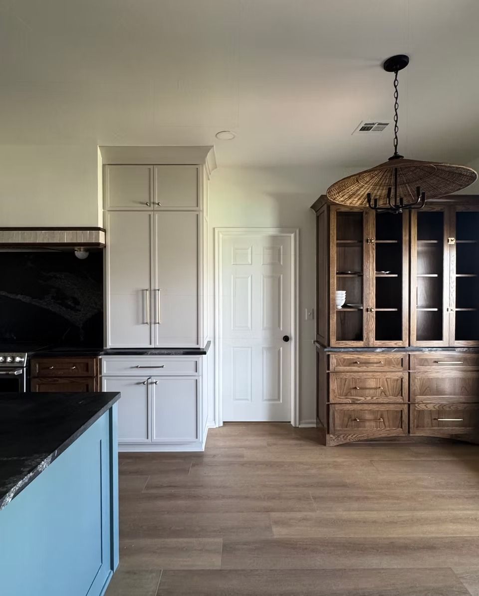 A kitchen interior with a blue island, cream cabinets, a white door, and a wooden hutch topped by a decorative lamp.