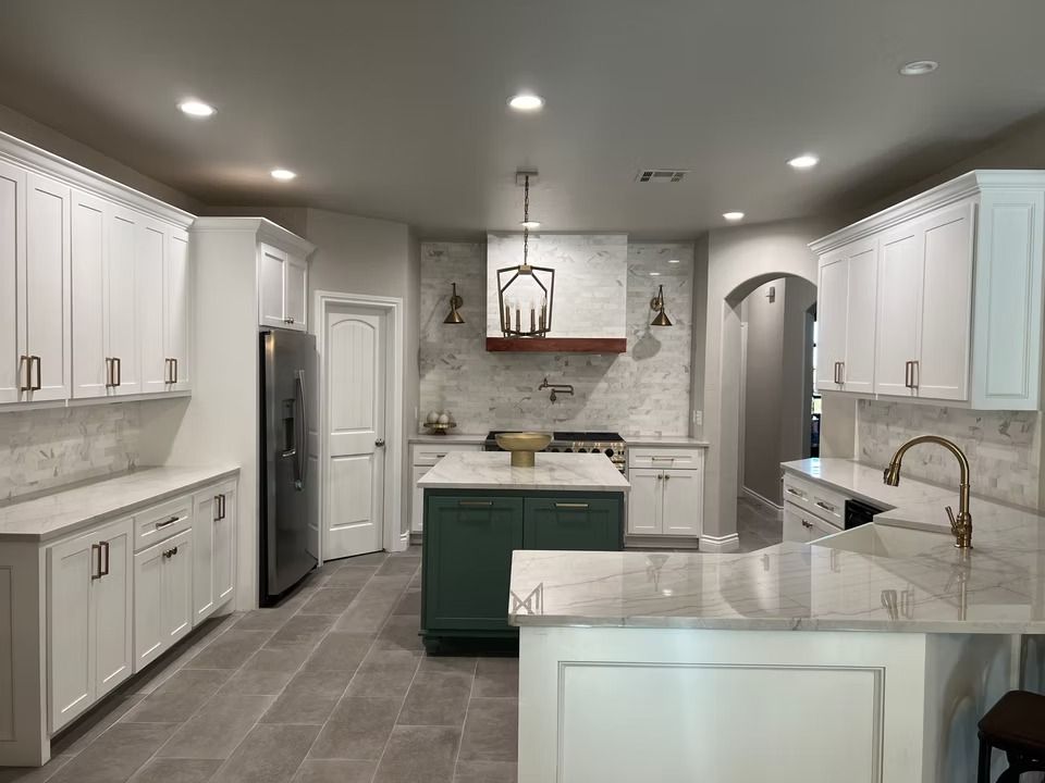 A spacious kitchen features white cabinets, a green central island, marble countertops, and a stainless steel refrigerator.
