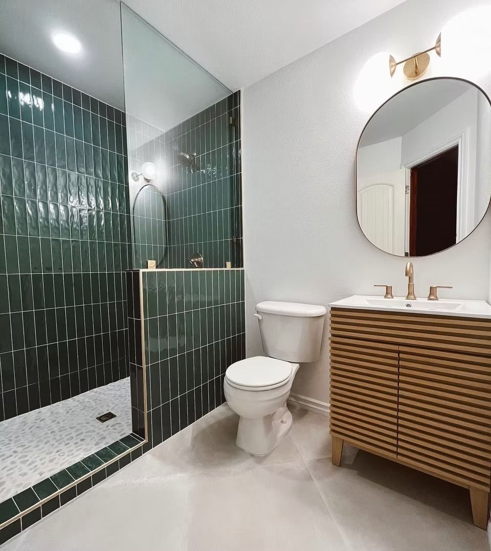 Modern bathroom with green subway-tiled shower, white toilet, oval mirror, and a textured wooden vanity.
