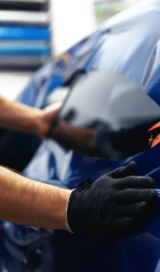 Hands in black gloves applying tinted film to a blue car window.