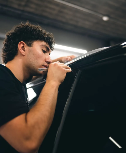 Person installing tint on a car window in a workshop.