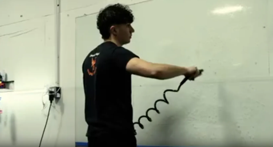 Man holding coiled black cord, standing in front of white board.