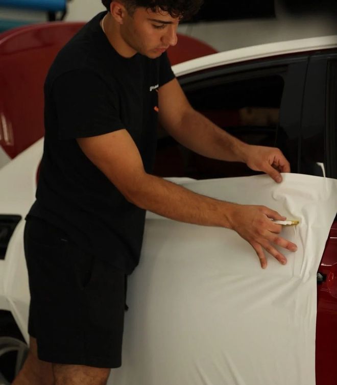 Person applying tint to a car window with a squeegee, soapy water visible, in an indoor setting.