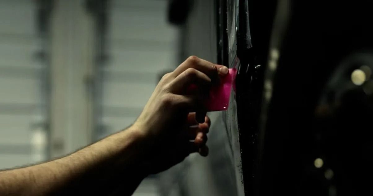 Hand holding a pink spray bottle, spraying a dark surface in a garage.