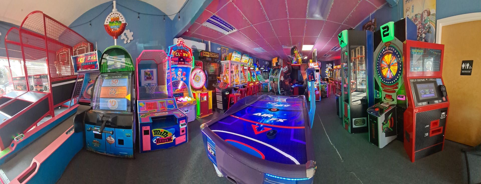 An arcade room with various game machines. Neon lights and a blue air hockey table are visible.