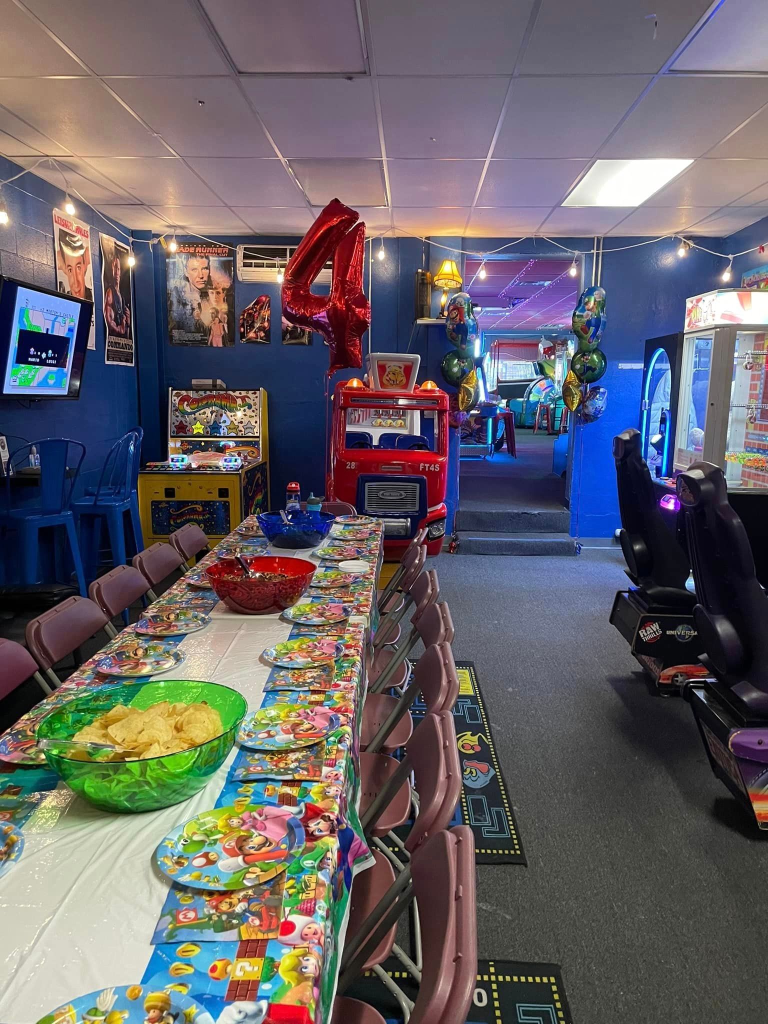 Arcade party room decorated for a fourth birthday. Table set with food, red number balloon.