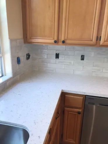 A kitchen with wooden cabinets , white counter tops , a sink , and a stainless steel dishwasher.