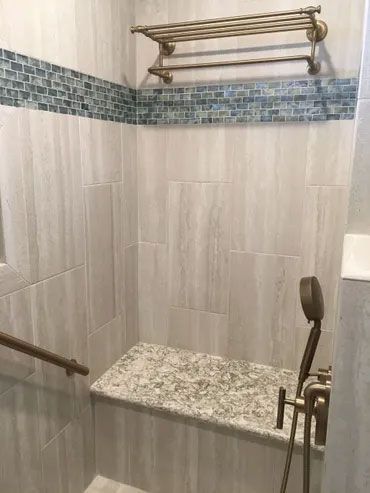 A bathroom with a walk in shower with a bench and a towel rack.
