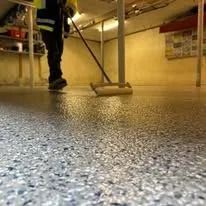 A worker uses a roller to apply a speckled epoxy coating to a floor in a basement.