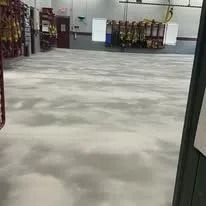 A vast, empty concrete floor in a fire station bay with hanging gear racks and a red door in the background.