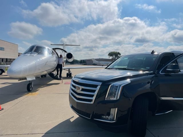 a cadillac is parked next to a private jet on a runway