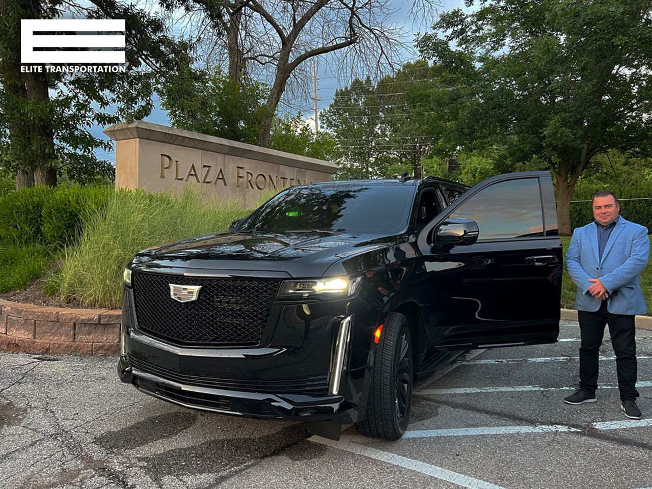 a man is standing next to a black cadillac escalade in a parking lot