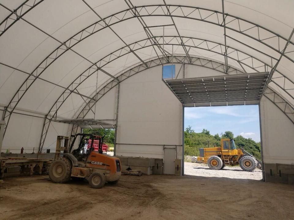 Large open warehouse with arched roof, two doors, and construction vehicles inside.