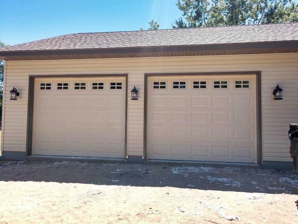 Two beige garage doors with lights, brown trim, and a brown roof.