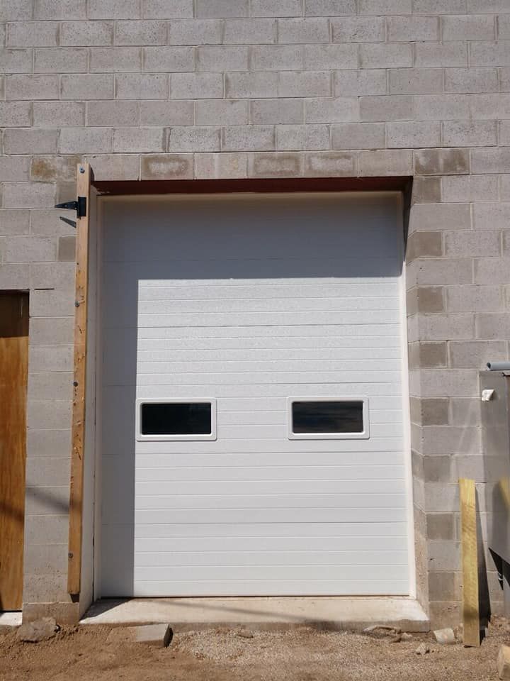 White garage door with two rectangular windows, set in a cinder block building.