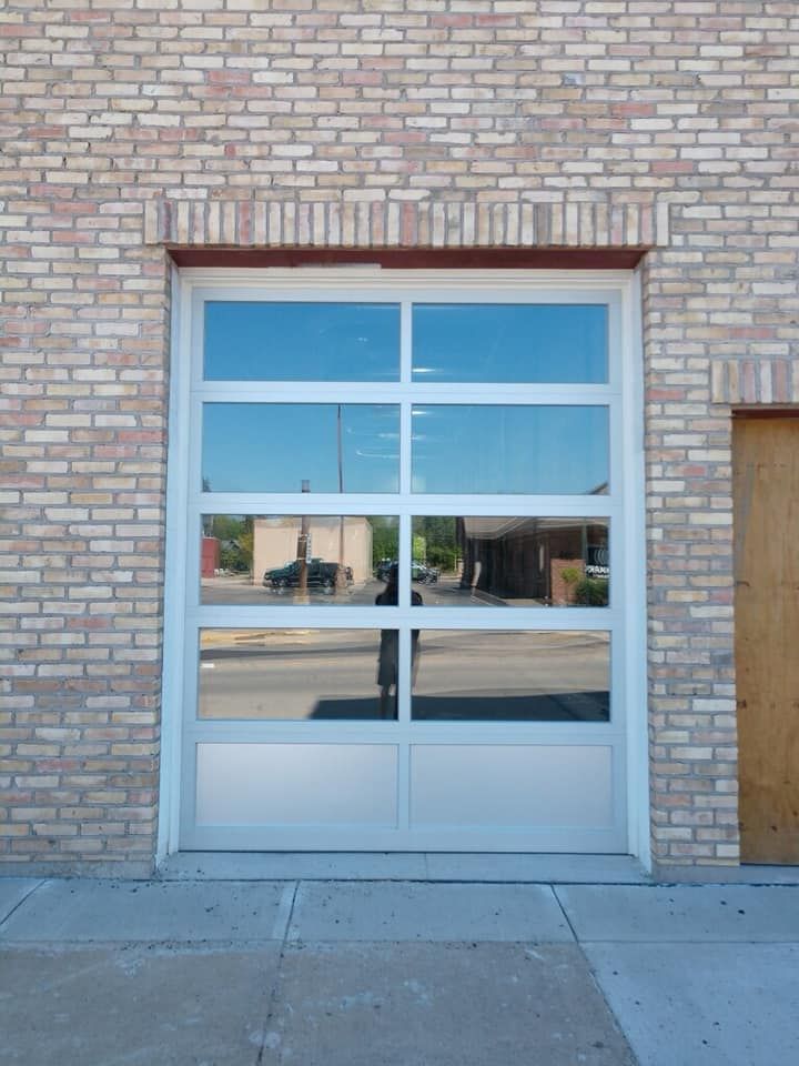 Glass garage door with white frame reflecting surrounding buildings, set in a brick wall.