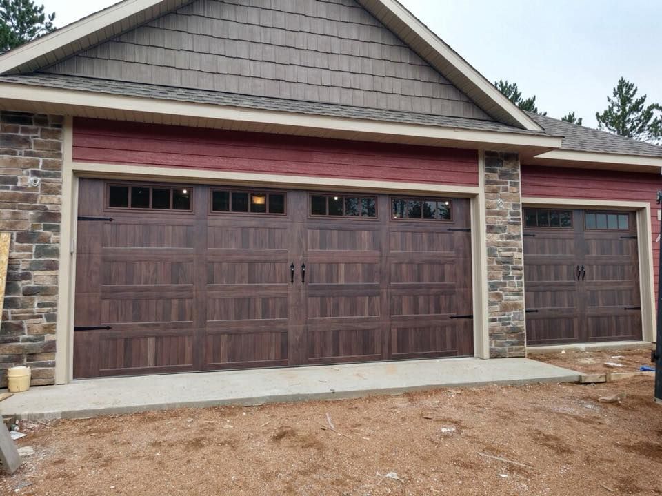Brown garage doors on a building with stone and red trim. Gray concrete slab.