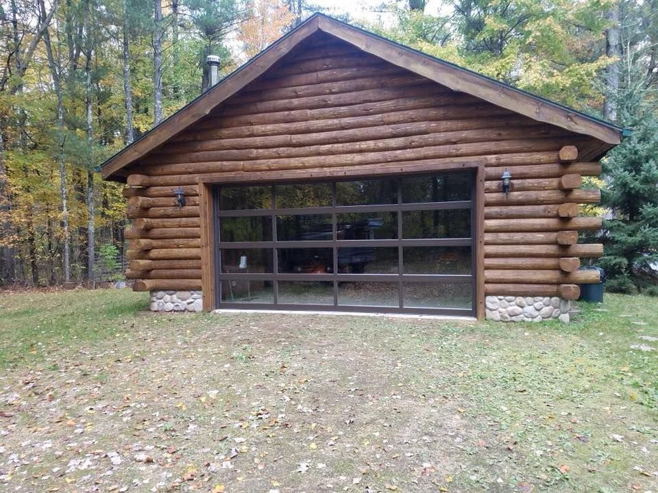 Log cabin-style garage with a large glass garage door, surrounded by trees and autumn leaves.