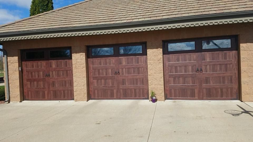 Three brown garage doors with windows, tan building exterior, concrete driveway.
