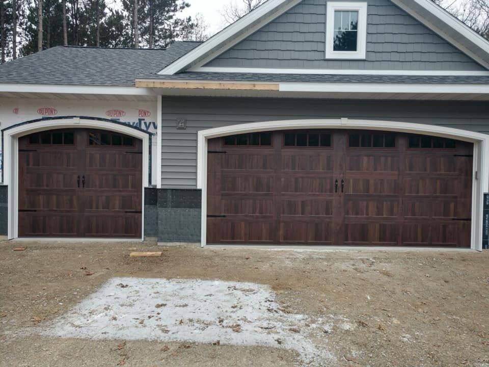 Brown garage doors on a house with gray siding; a small window in the gable.