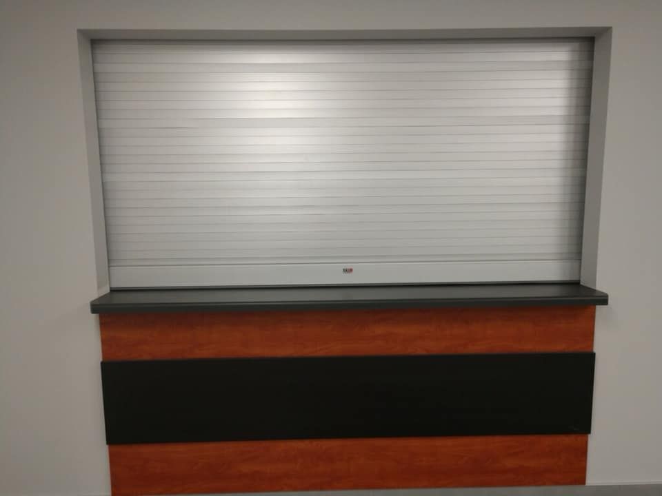 A counter with a closed, rolling metal shutter above. The counter has a black and brown panel.