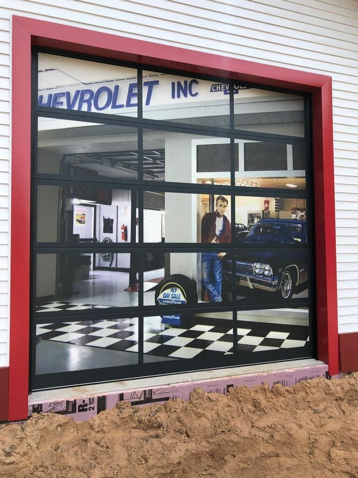 Glass garage door reflecting a Chevrolet dealership interior, black checkered floor, red trim.