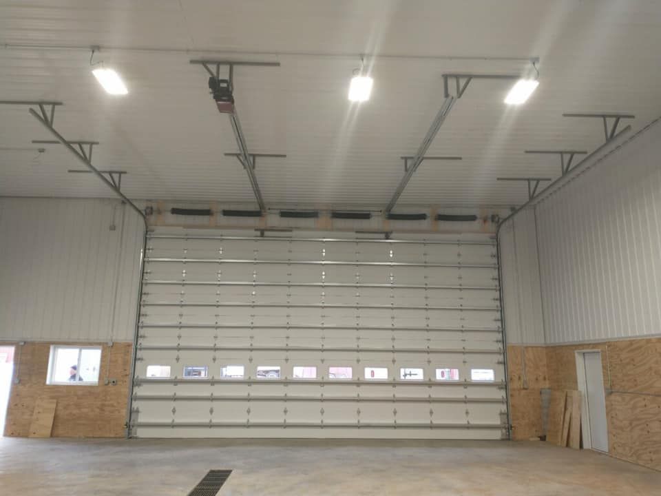 Interior of a large garage with a closed overhead door, lights, and concrete floor.