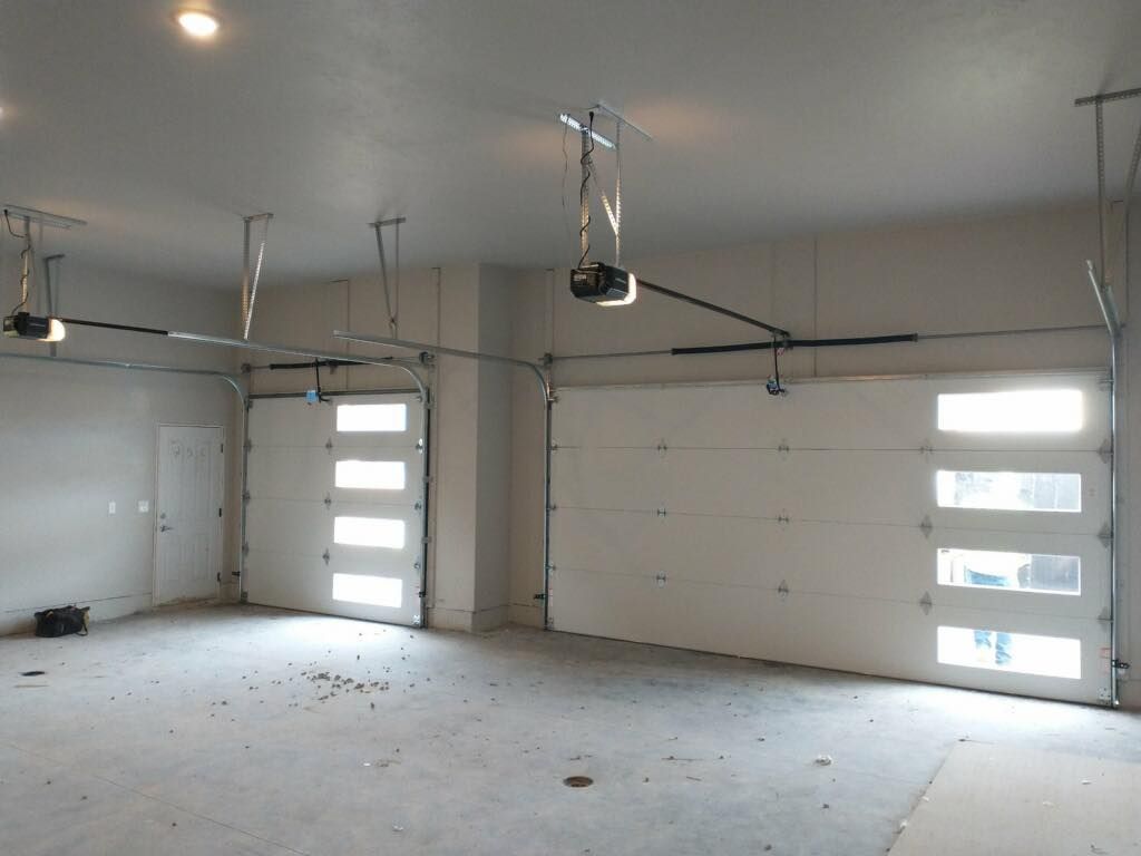 An empty garage with two closed white doors, a white door in the far left corner, and a gray concrete floor.