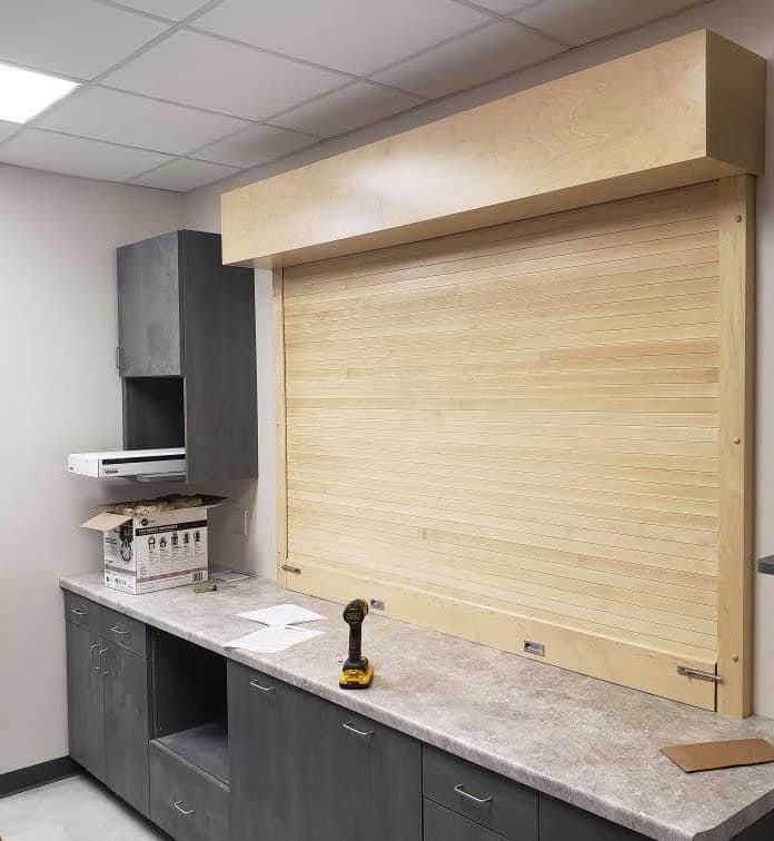 Wooden roll-up door above a countertop with gray cabinets. A drill sits on the countertop.