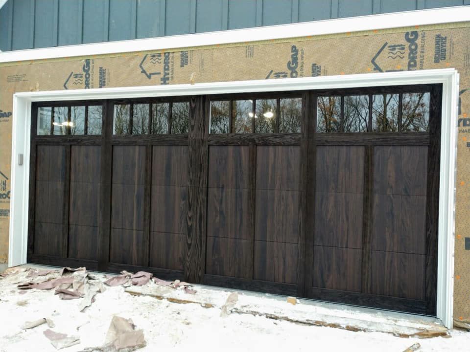 Dark wood garage door with small glass panels, installed on a building under construction, snow on the ground.