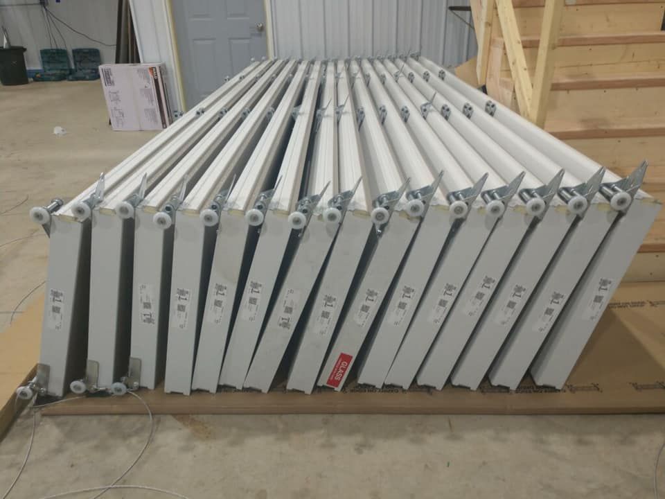 Stack of white metal doors with rollers, leaning against each other in a building. Numbered labels are visible.