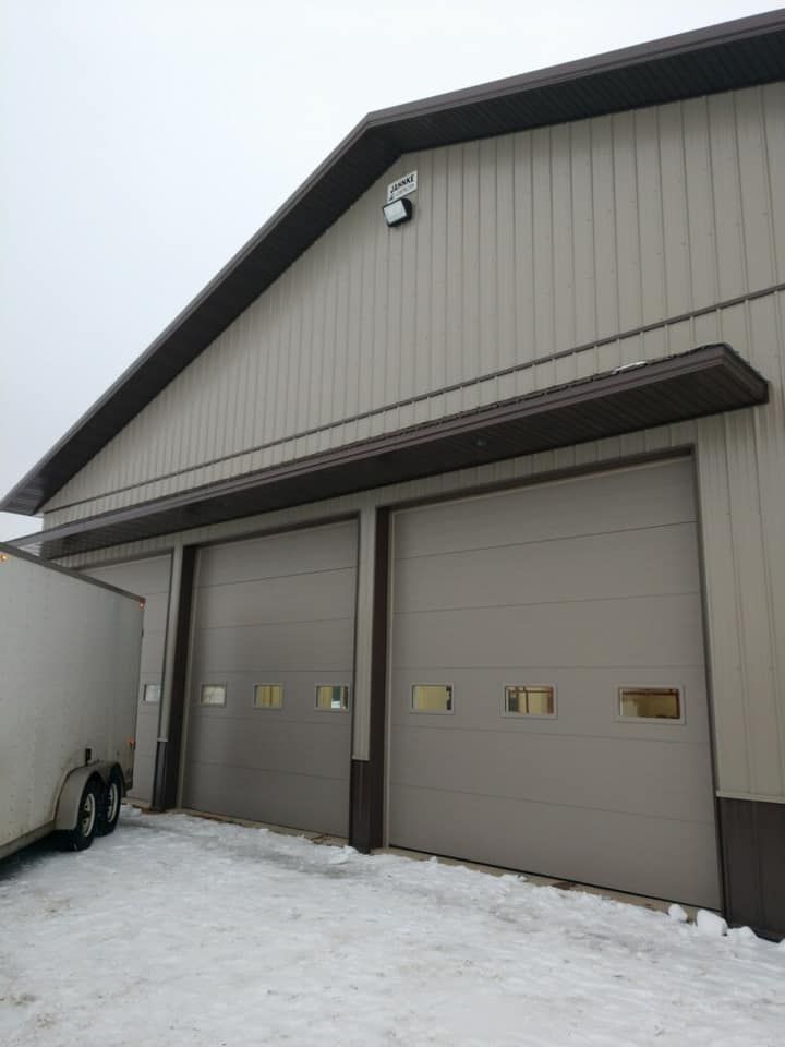 Tan commercial building with two garage doors and brown trim, snow on ground.
