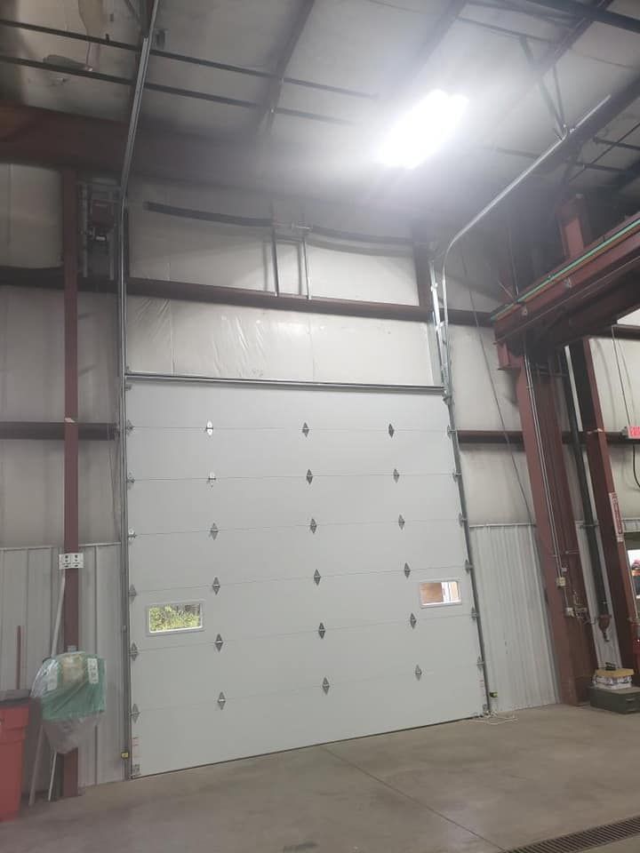 White closed garage door inside a commercial building. Metal frame, overhead lighting, concrete floor.