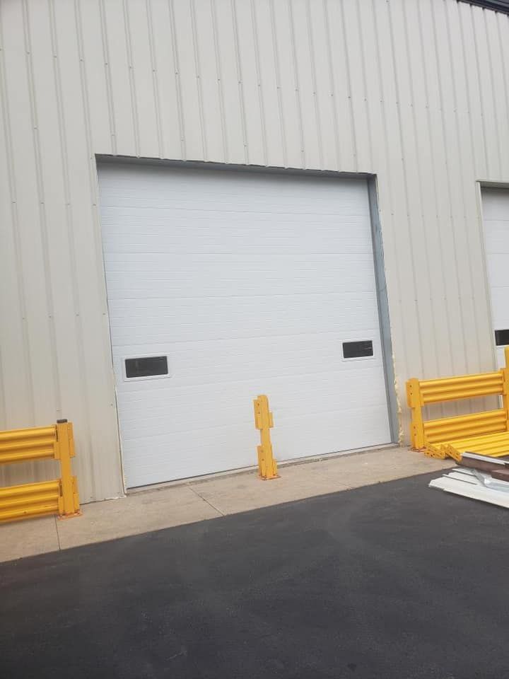 White warehouse loading dock door with black handles, yellow safety barriers, and a gray concrete surface.