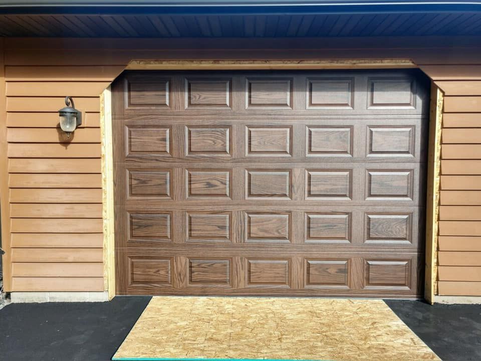 Brown garage door with a wood-look finish, set in a brown building with a light fixture on the left.
