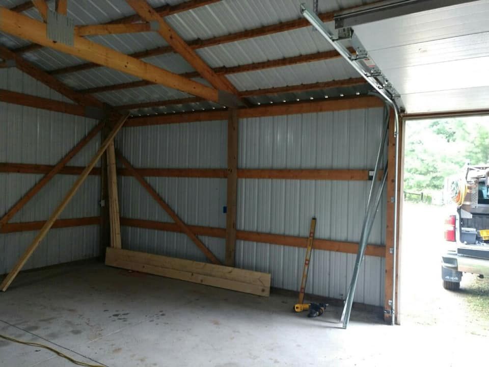 Interior of a metal-sided pole barn with open door. Metal track for a garage door runs along the ceiling.