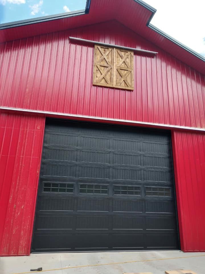 Red barn with black garage door and decorative wooden shutters.
