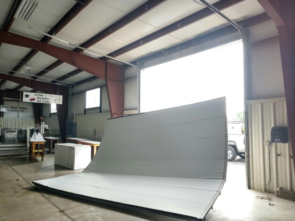 A large, bent, gray wall section inside a warehouse with an open door.