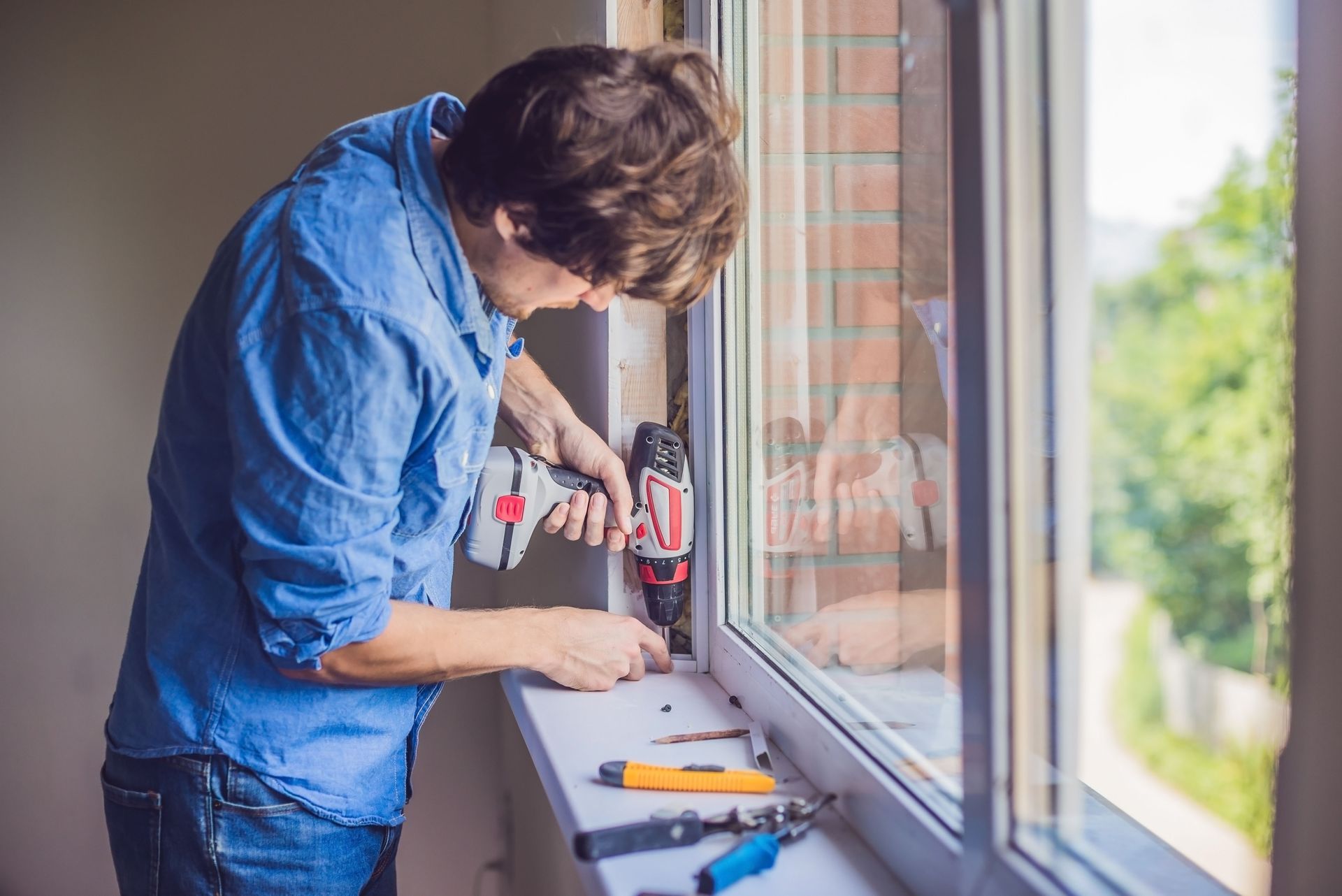 Man in blue shirt using a power drill to install a window.